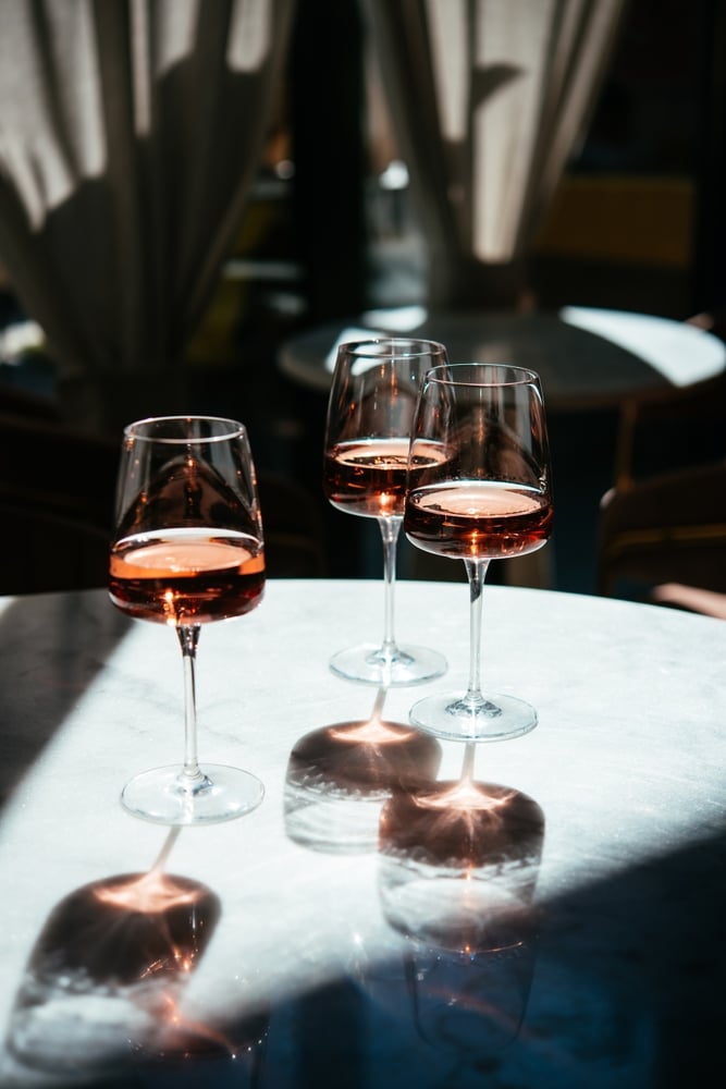 Verres de rosé: l'éclat du vin à la lumière du soleil. Trois verres de vin rosé sur une table en marbre. La lumière du soleil intense projette des ombres et reflets ambrés.