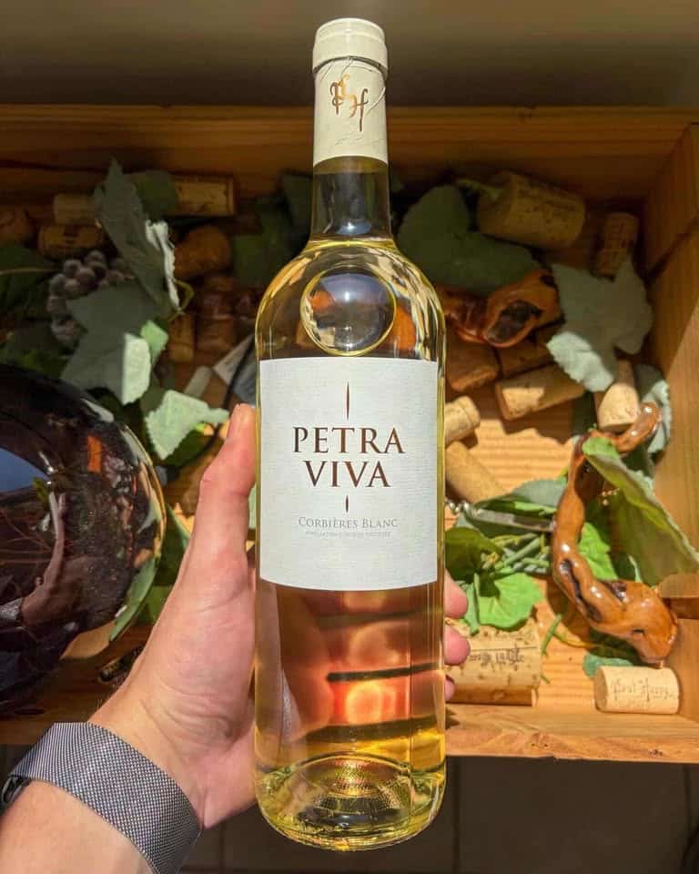 Bouteille de vin blanc Petra Viva Corbières Blanc tenue devant une caisse de bouchons de liège.